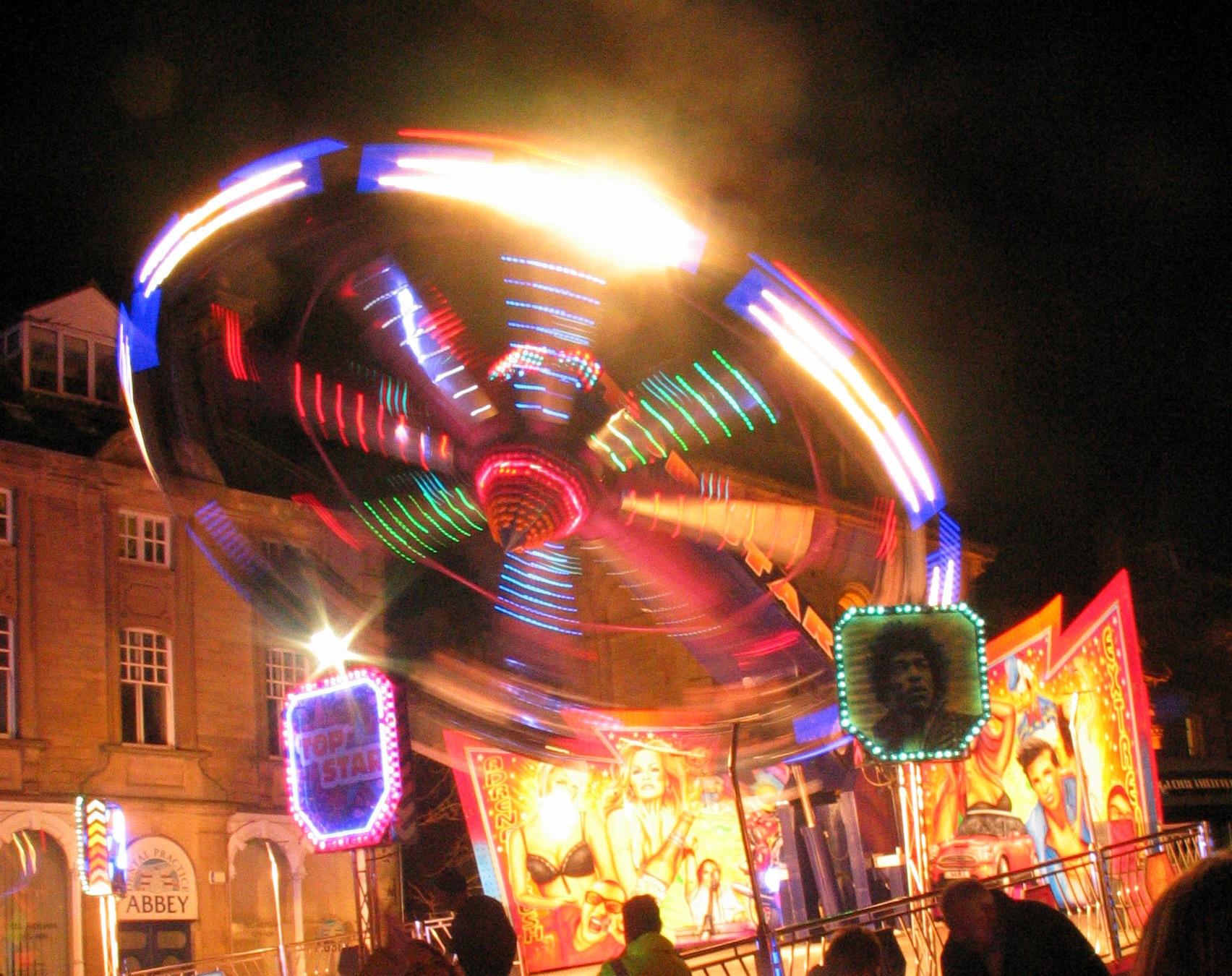 Neon funfair ride lighting up the night sky in a multicoloured circle. Image by Roger Clegg